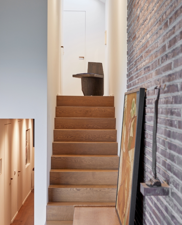View of a wooden staircase with a Norki design stool and brick wall