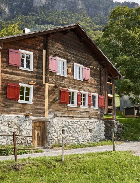Chalet montagnard traditionnel en vieux bois fleuri sous un ciel d'été ensoleillé