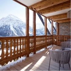 Balcon en bois sculpté d'un chalet offrant une vue majestueuse sur des massifs enneigés d'Arosa