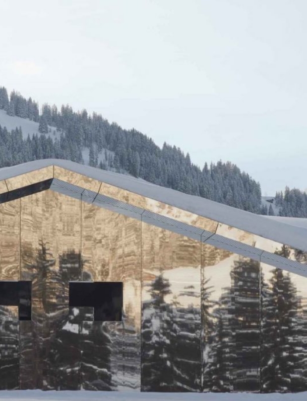 Modern chalet with mirrored surfaces reflecting the snowy alpine environment